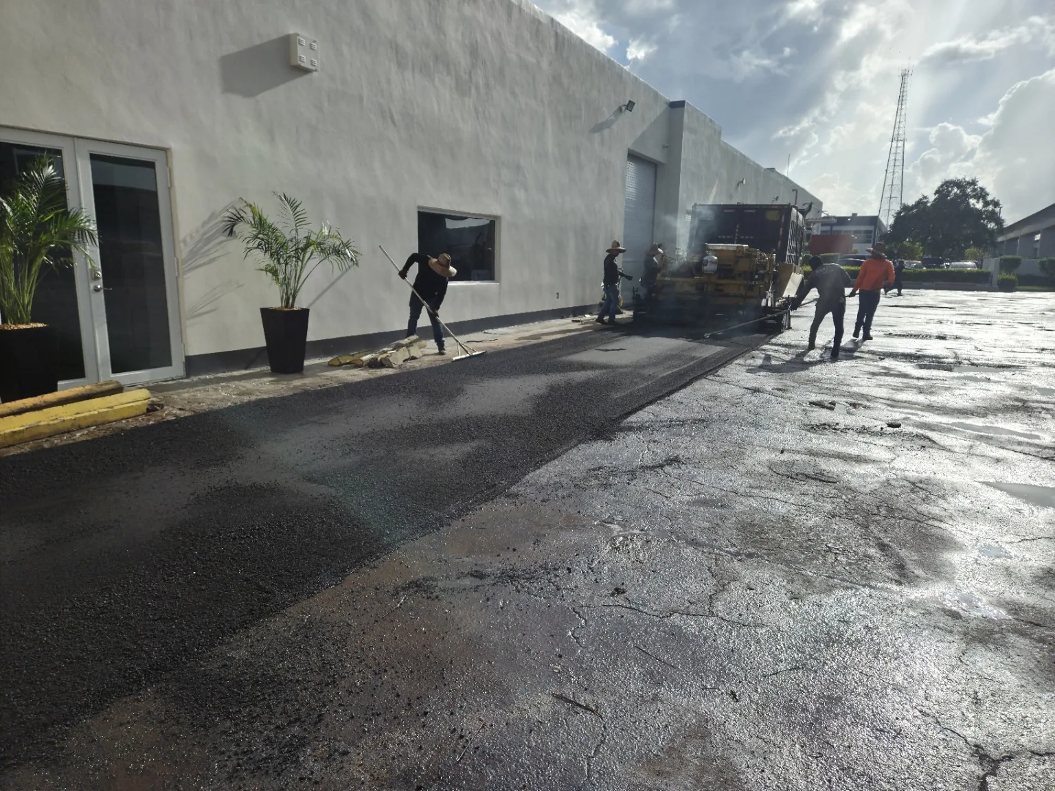 Paving crew installing asphalt along a commercial building